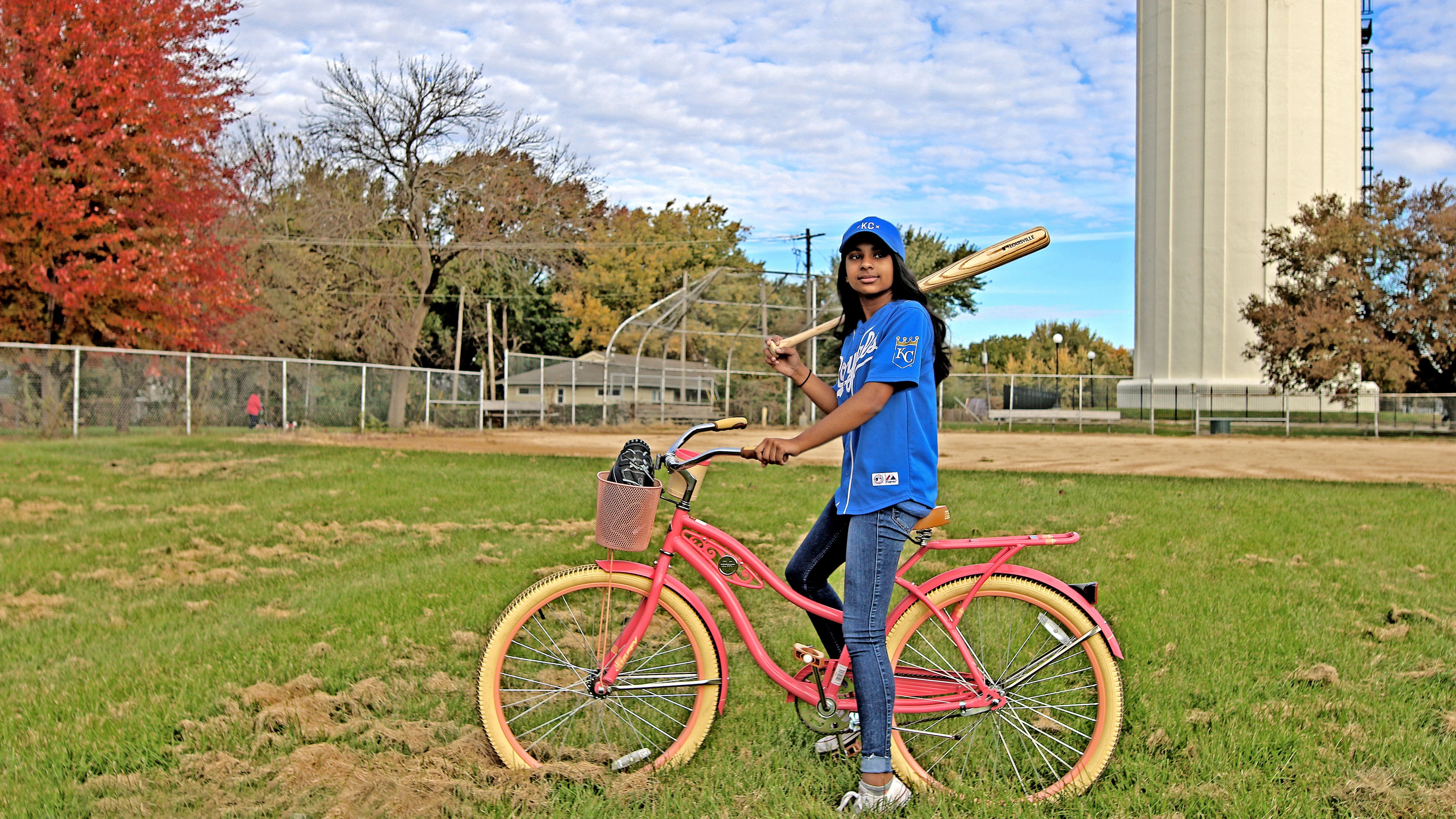 Girl posing with a baseball bat and a bike